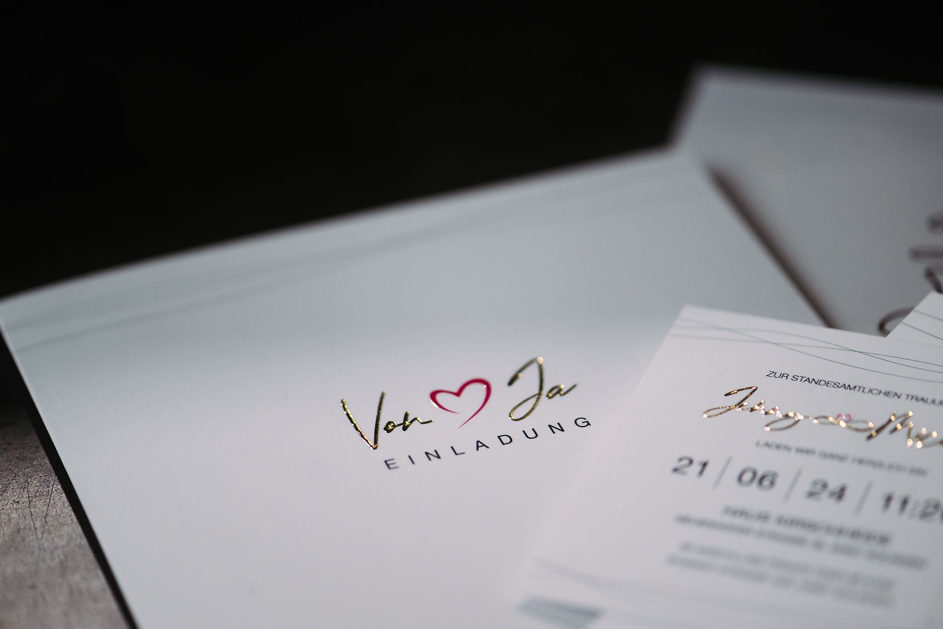 Elegante Hochzeitseinladung mit Glamprint in gold und einem Herzsymbol, das relieflackiert ist.