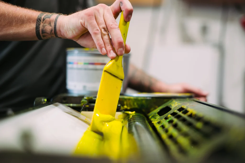 Mit einer Spachtel wird gelbe Druckfarbe auf die Rollen der Offsetmaschine aufgebracht.