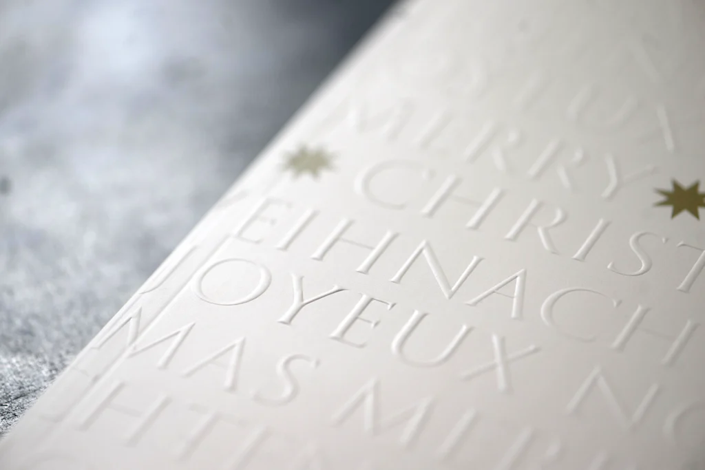 Weihnachtskarte mit Blindprägung und goldenen Sternen in edlem Design.“