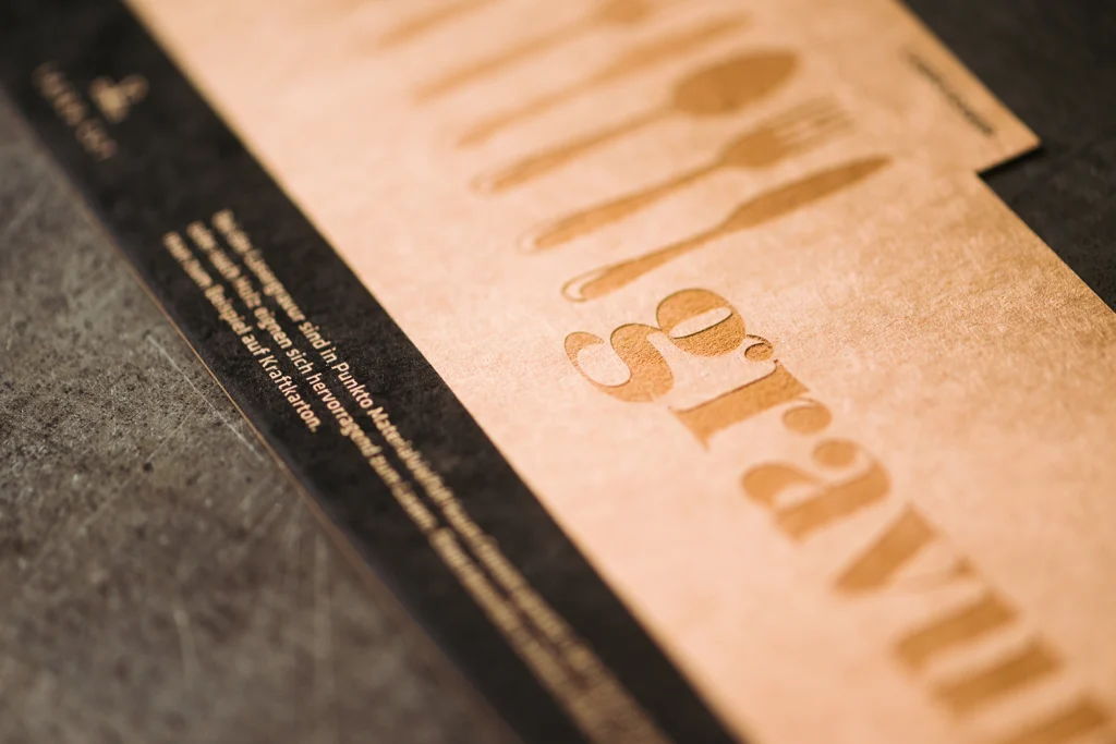 Menükarte mit Lasergravur von Besteck und Schriftzug auf braunem Naturpapier.