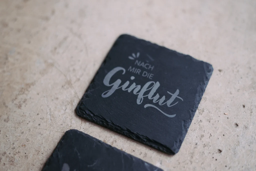 Schieferuntersetzer mit Lasergravur ‚Nach mir die Ginflut‘ in moderner Typografie.